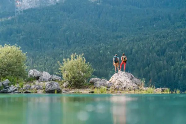 Two people are standing on a rock by a body of water.