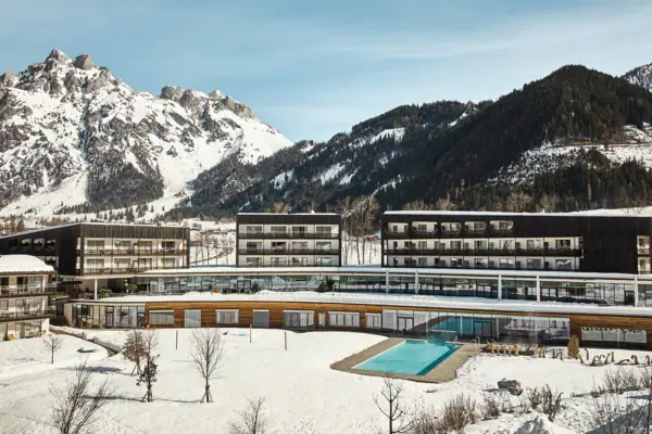 The hotel building with the outdoor pool in the snow, surrounded by mountains.