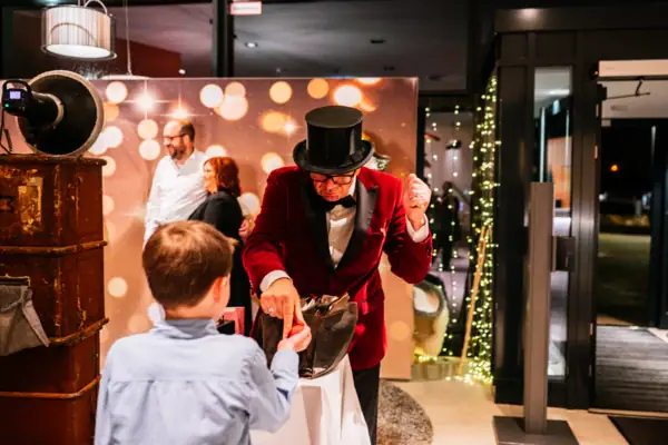 A man in a red suit hands a knotted balloon to a boy.