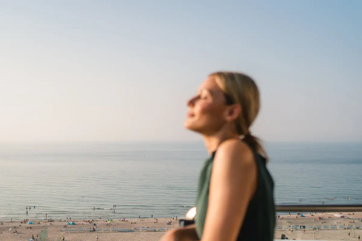 A woman stands on a railing and looks out over a beach.