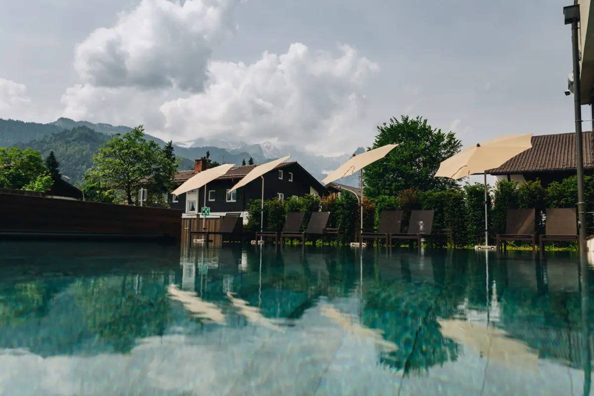A swimming pool with chairs and parasols in front of houses.