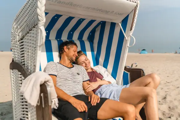A man and a woman are lying in a beach chair on the beach.