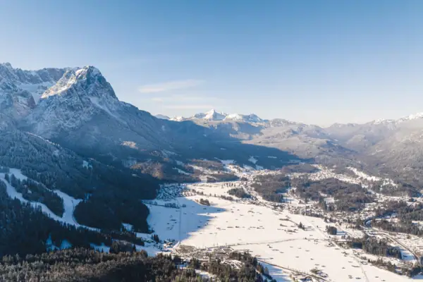 Verschneite Berglandschaft mit einer Stadt und Bäumen.