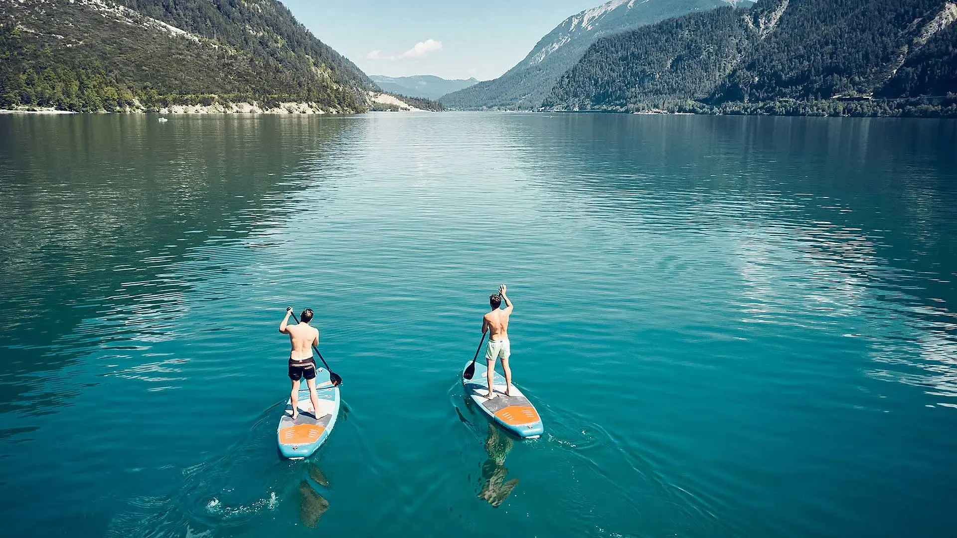 Two men on paddleboards on a lake with mountains in the background.