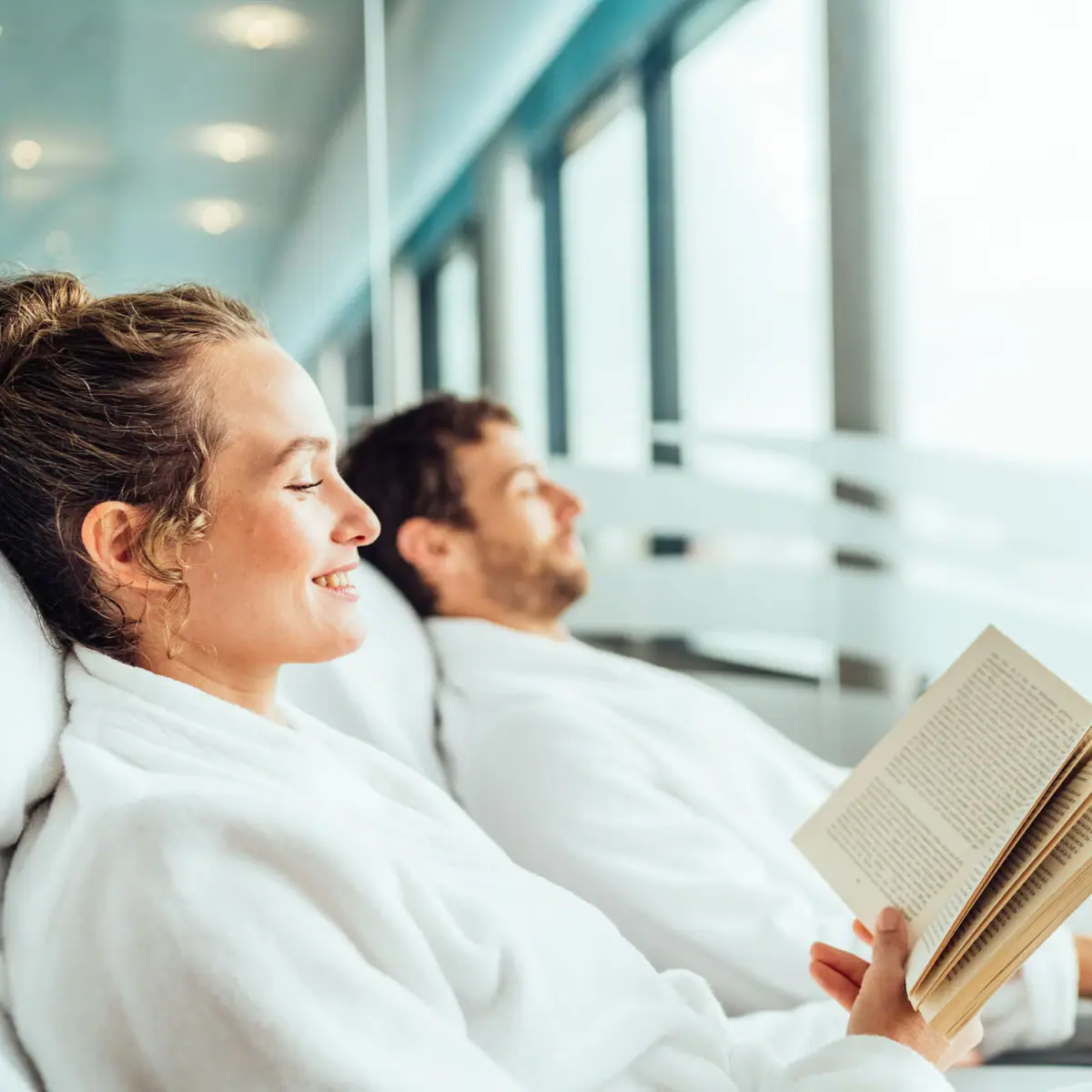 A man and a woman in bathrobes are reading a book.