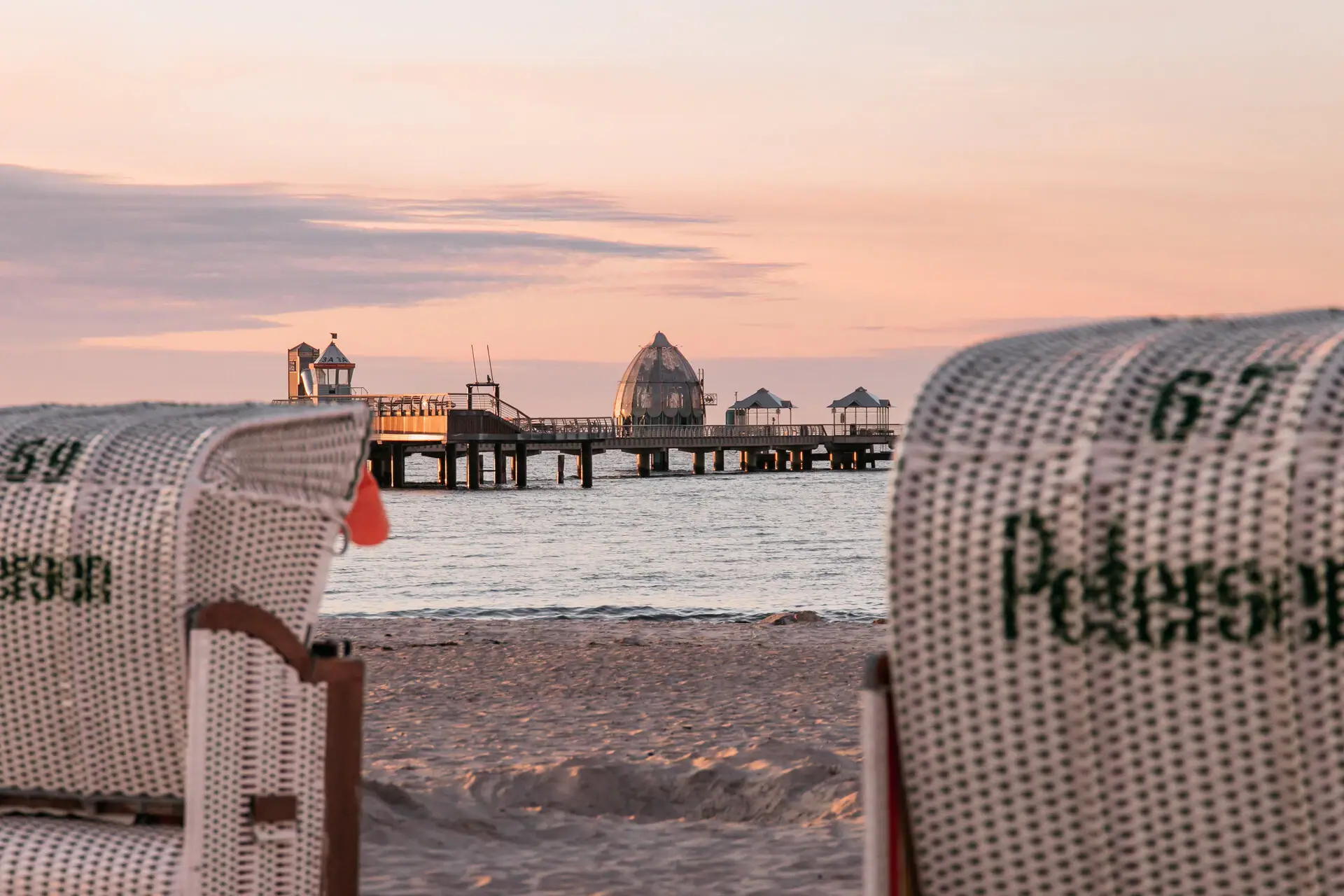 A beach chair on the beach with a pier in the background.