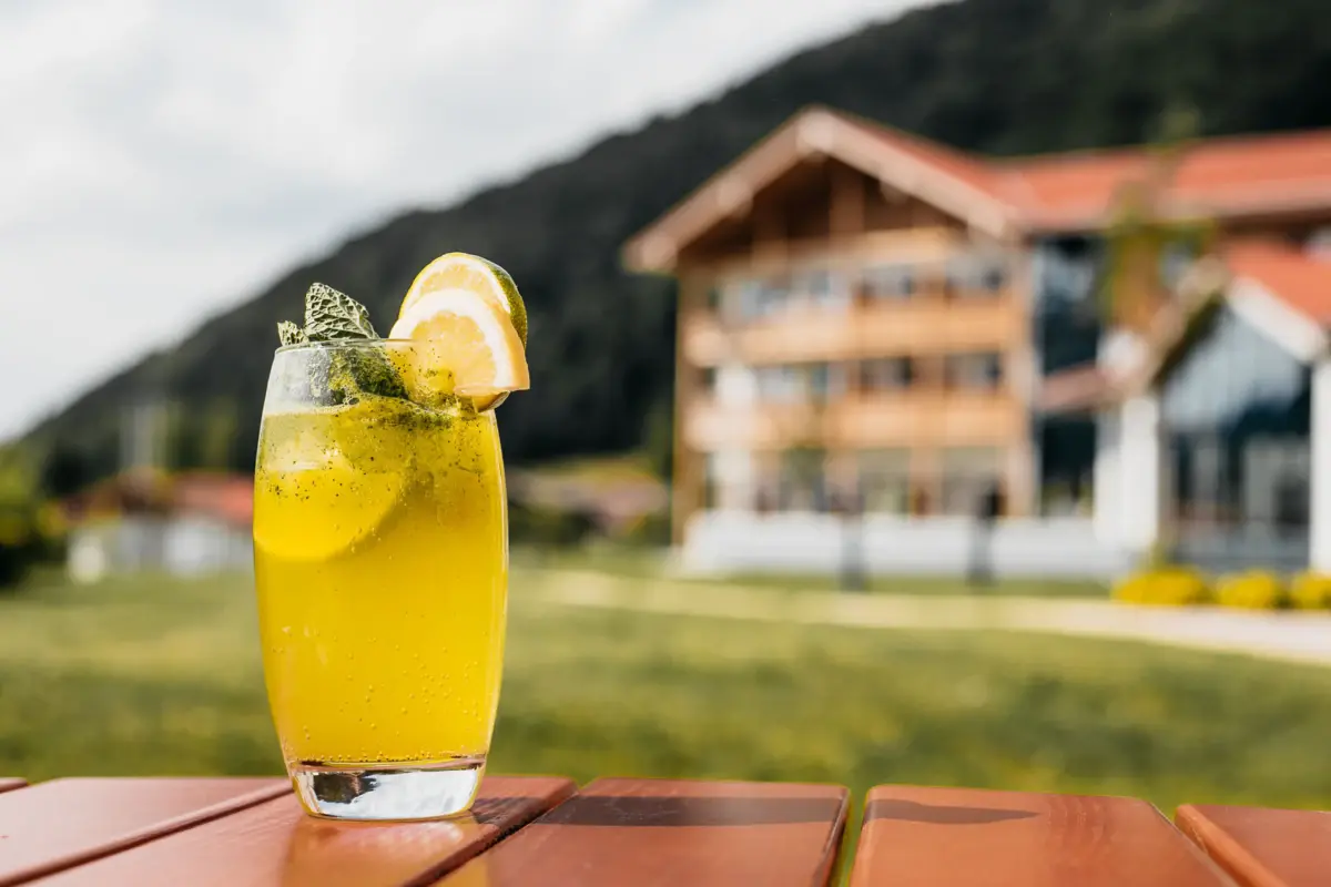 A glass of yellow liquid, garnished with a slice of lemon and mint, on a table.