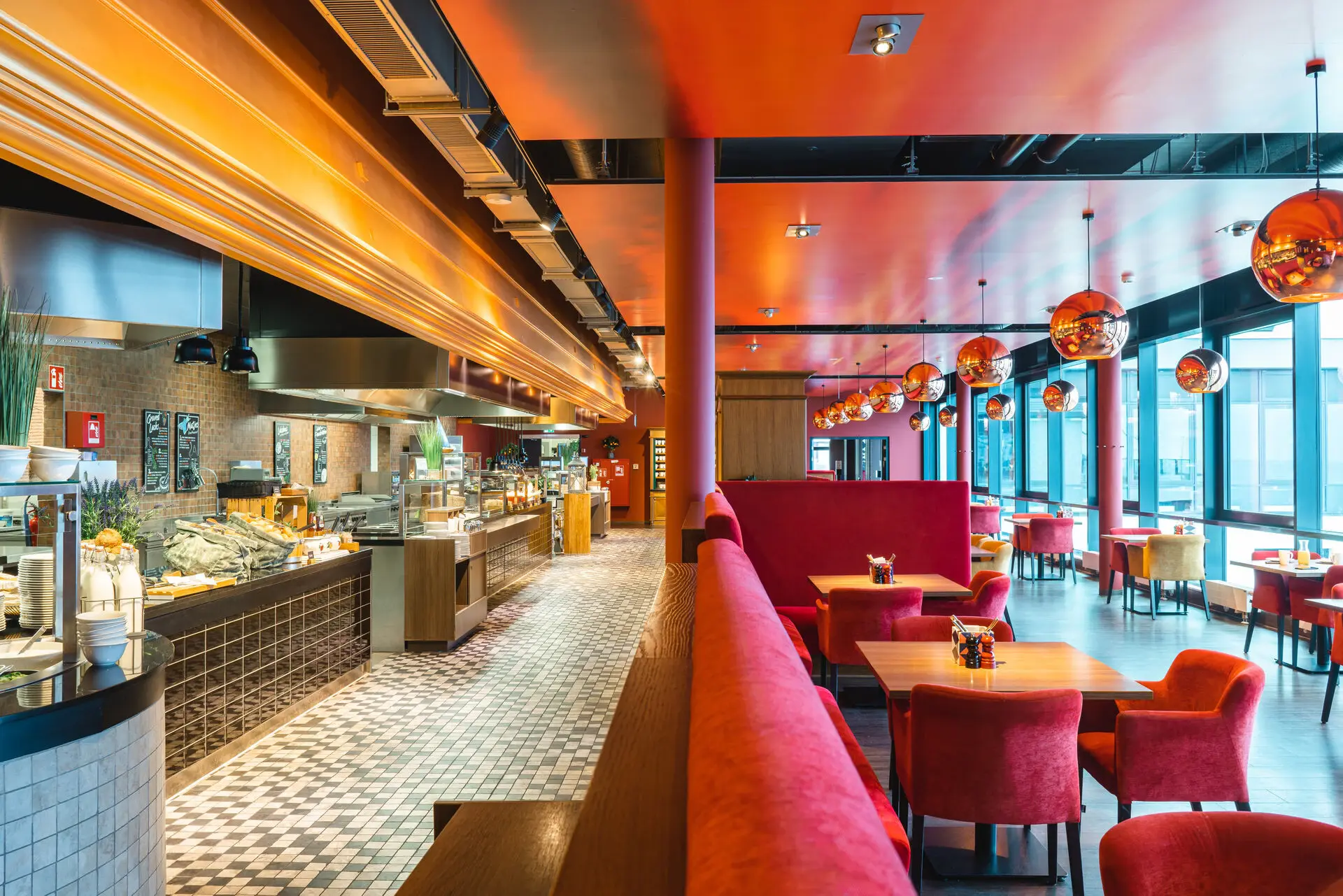 Restaurant interior with red couches and tables in front of a buffet of various dishes on the side