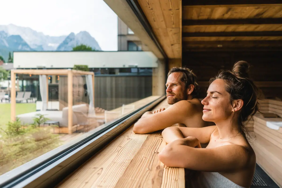 Sauna Aja, Garmisch-Partenkirchen A man and a woman are leaning against a window in a sauna at a wellness hotel in Bavaria.