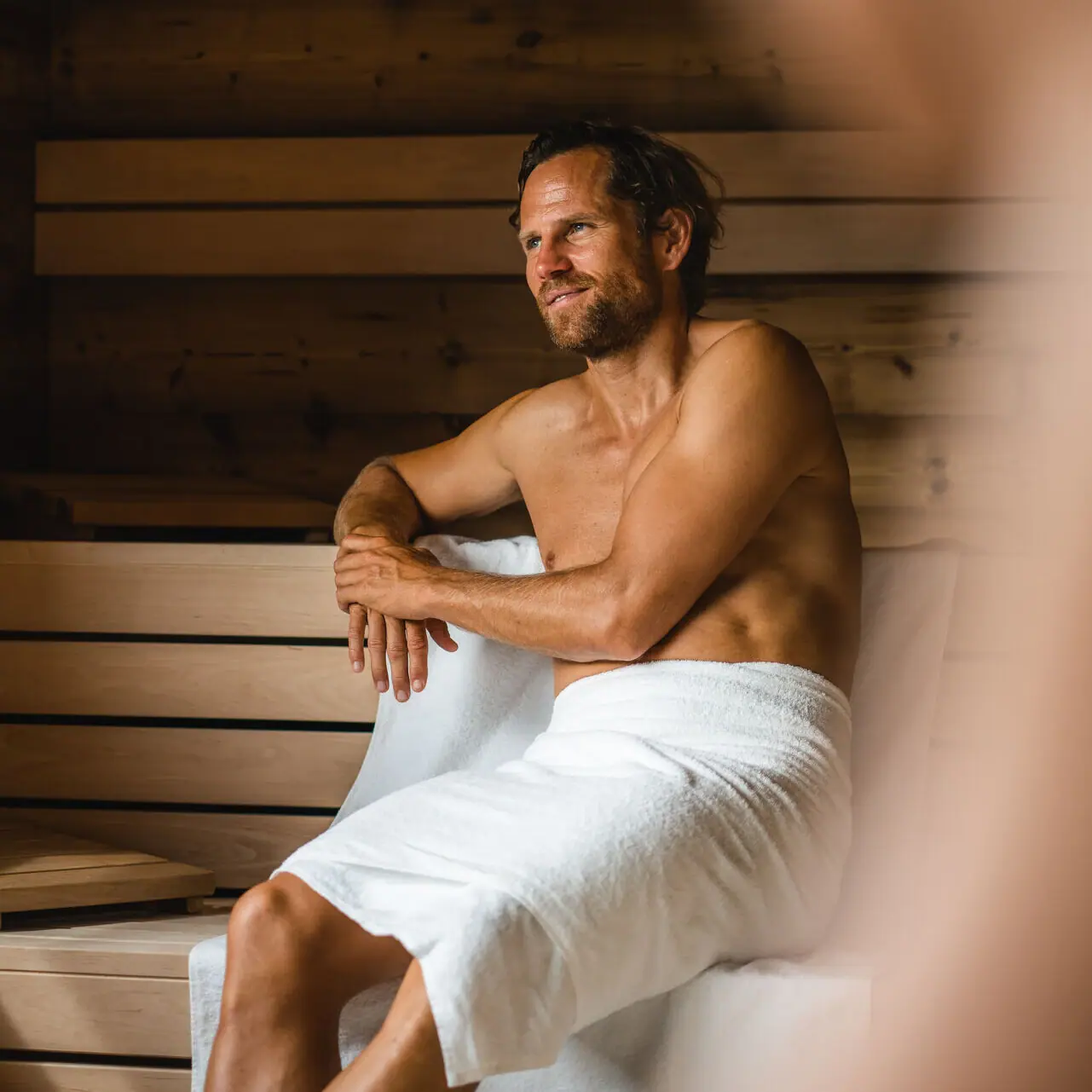 A man sits in the sauna at aja Garmisch-Partenkirchen with a towel.