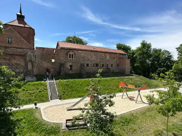 Visit Beeskow Castle A playground in front of a building with trees and a blue sky.