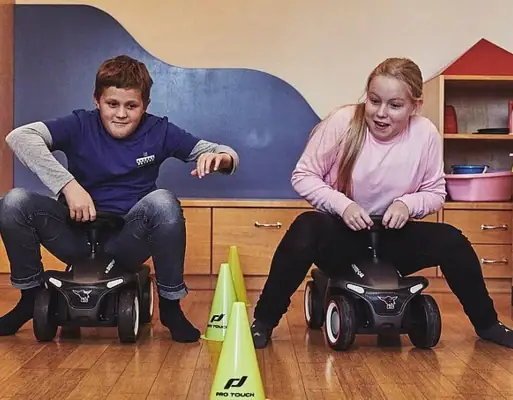 A boy and a girl sit on toy cars.