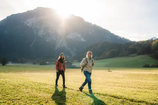 Chiemgau Two women walking in a field with mountains in the background.