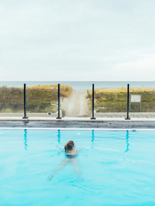 Outdoor pool at the aja Warnemünde A woman swims in a pool with the sea in the background.