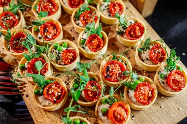 A tray with various dishes with small tomatoes and salad on a wooden surface.