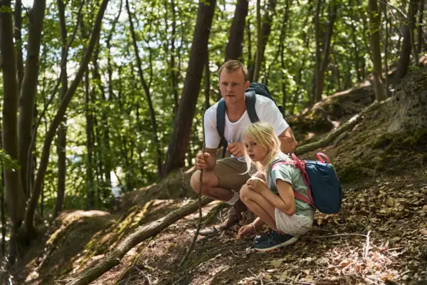 A man and a girl are sitting on a hill in the forest.