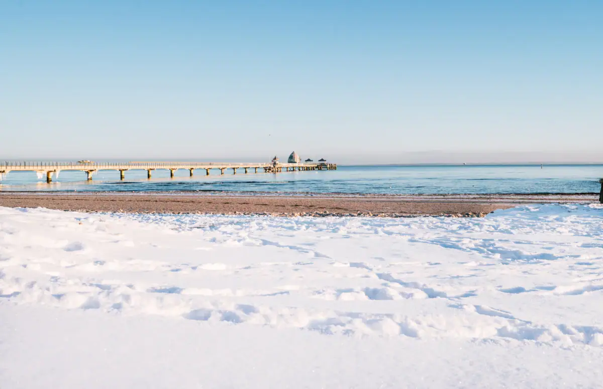 A snow-covered beach with a jetty and water in winter.