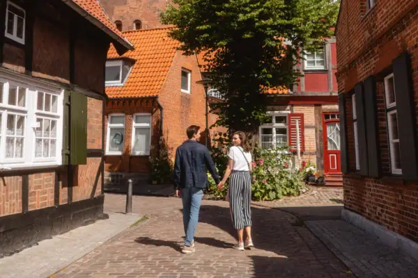 Old Town Travemünde A man and a woman hold hands in a courtyard with brick buildings.