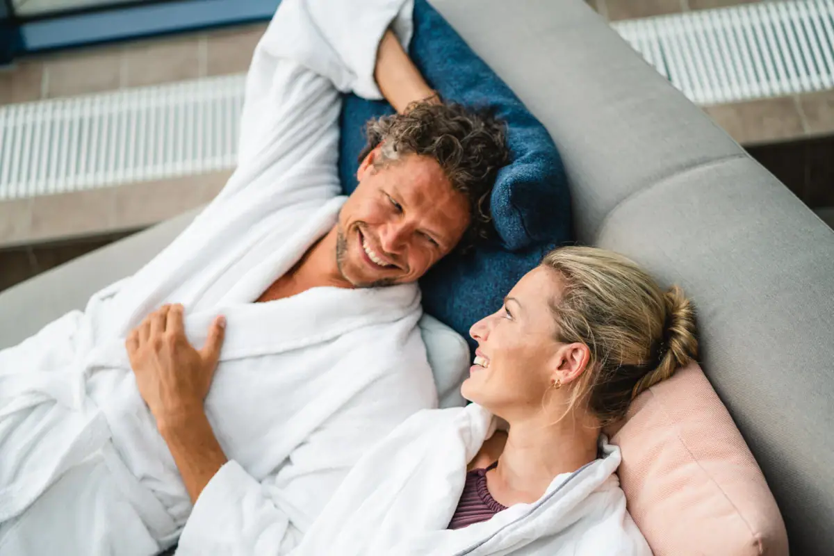 A man and a woman lie smiling on a sofa.