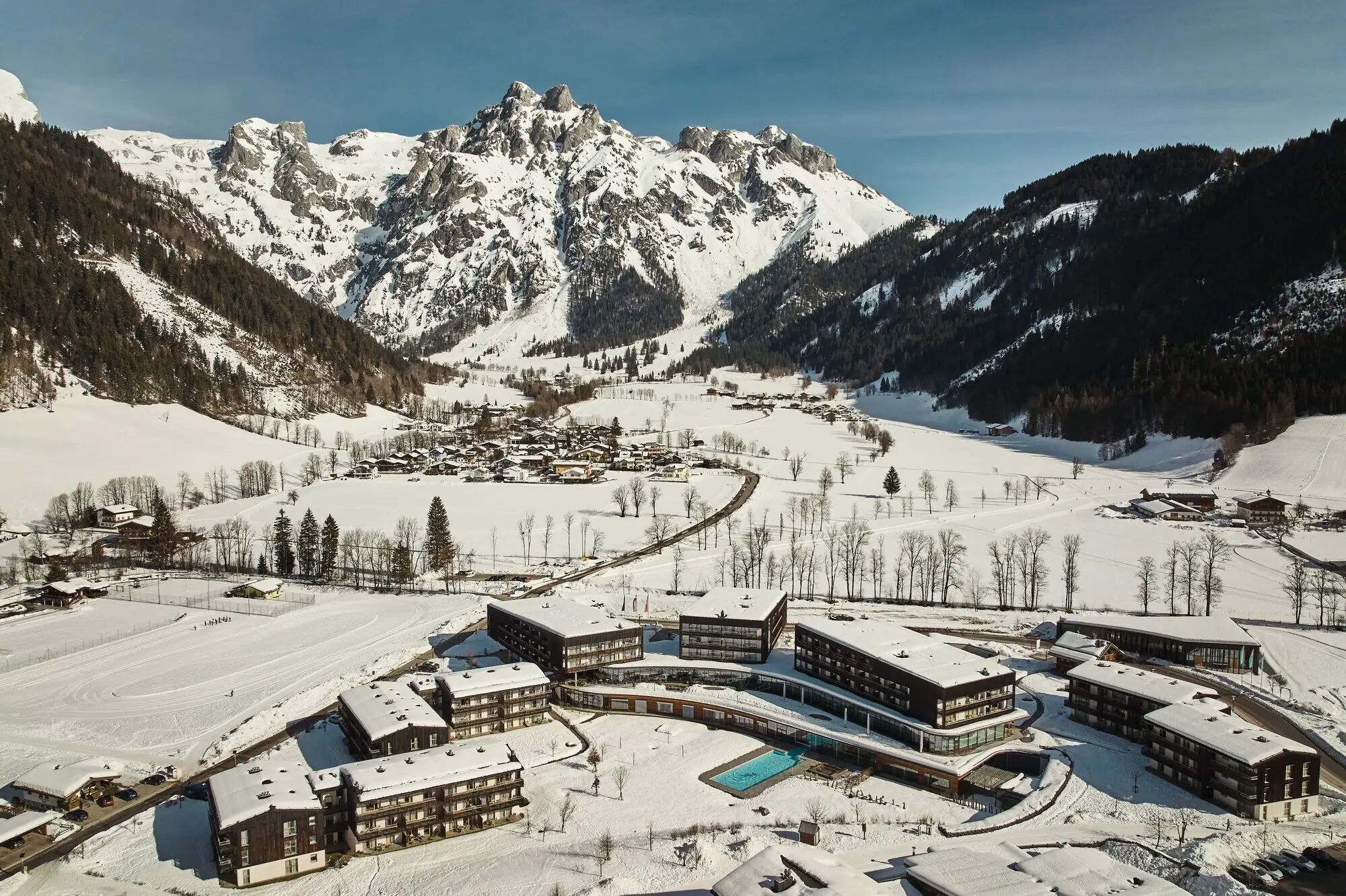 Group of buildings in a snowy valley with a mountain backdrop.