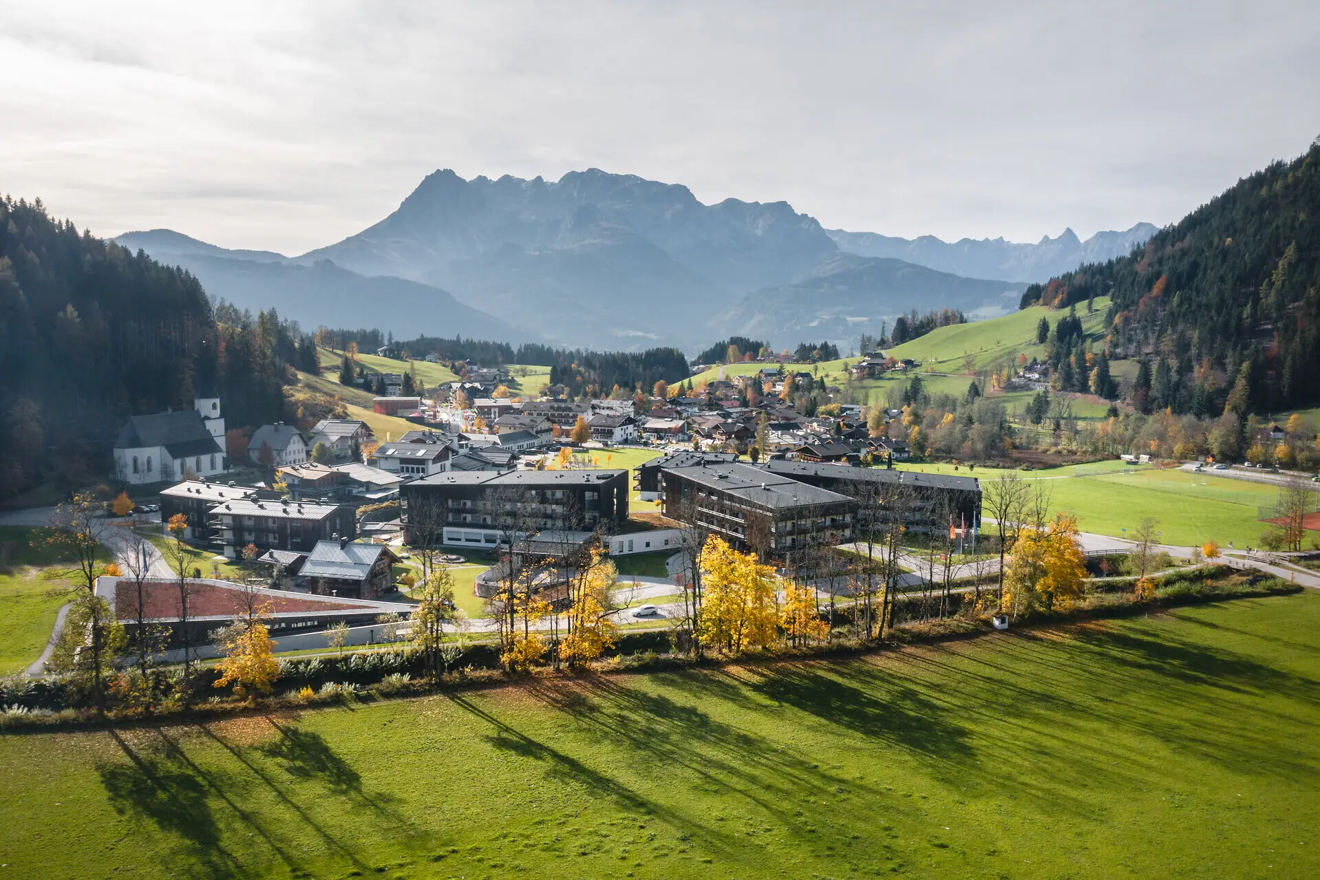 Town in a valley with mountains in the background, surrounded by grassland and trees.