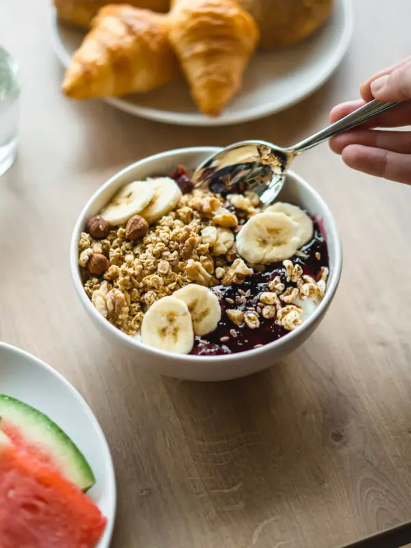 A bowl of granola, fruit and a spoon.