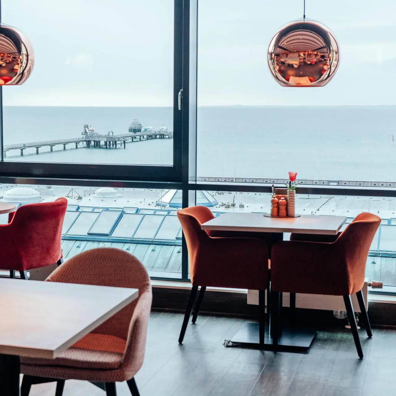 A room with a view of the ocean and a pier through large windows.