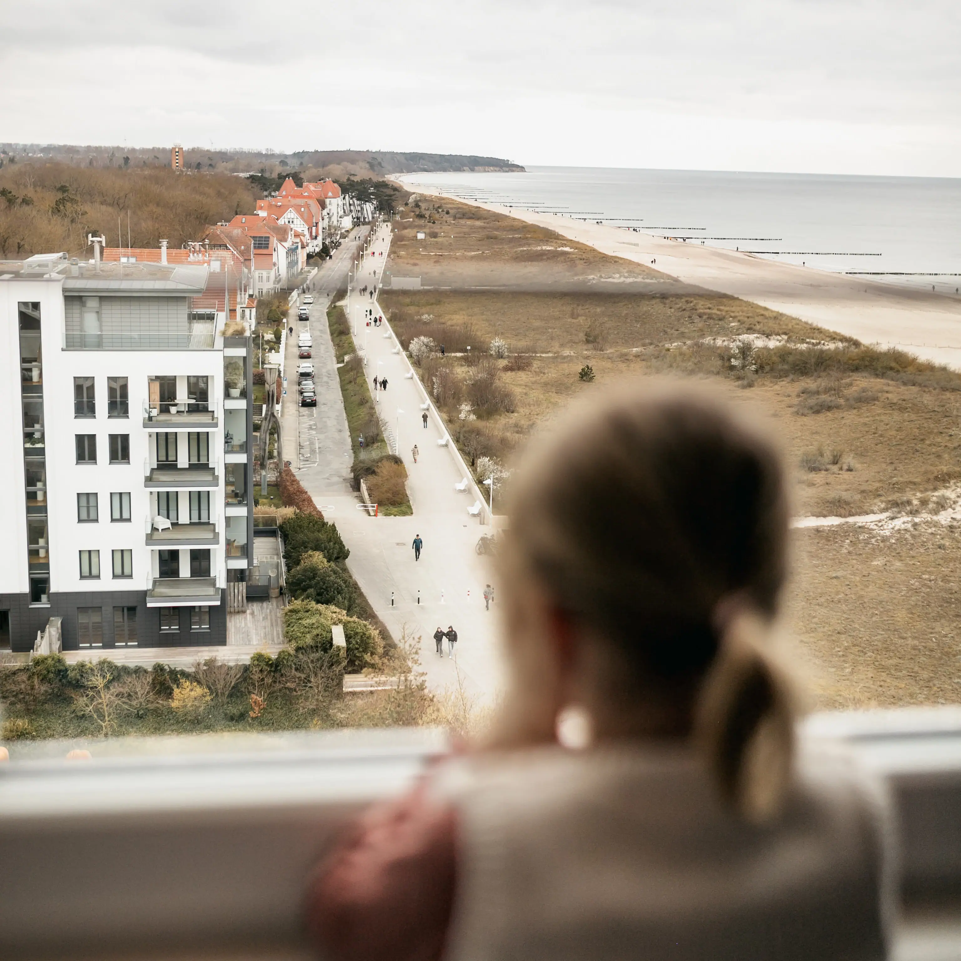 A girl is looking out of a window at a beach.