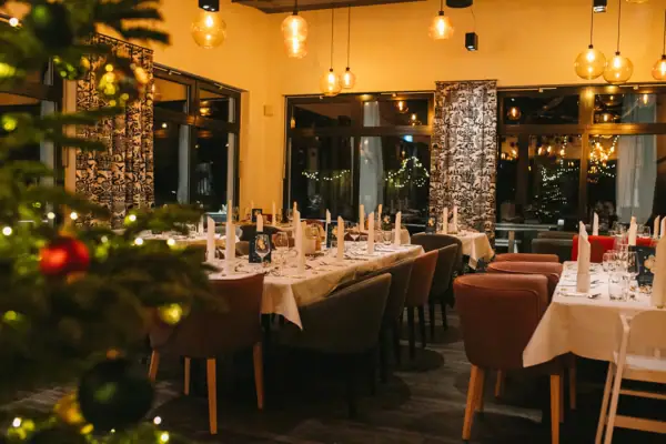 A room with tables and chairs, festively decorated and a Christmas tree in the foreground in the blur.