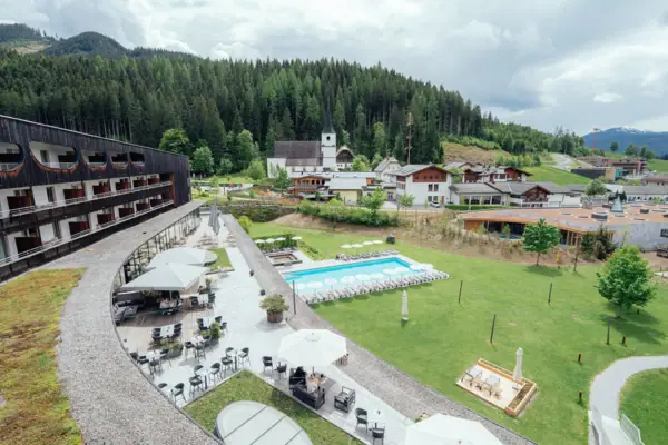 A building with a swimming pool in the foreground and trees in the background.