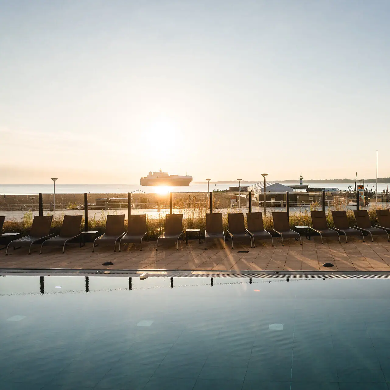 Outdoor pool aja Travemünde A pool with chairs and a boat in the background.