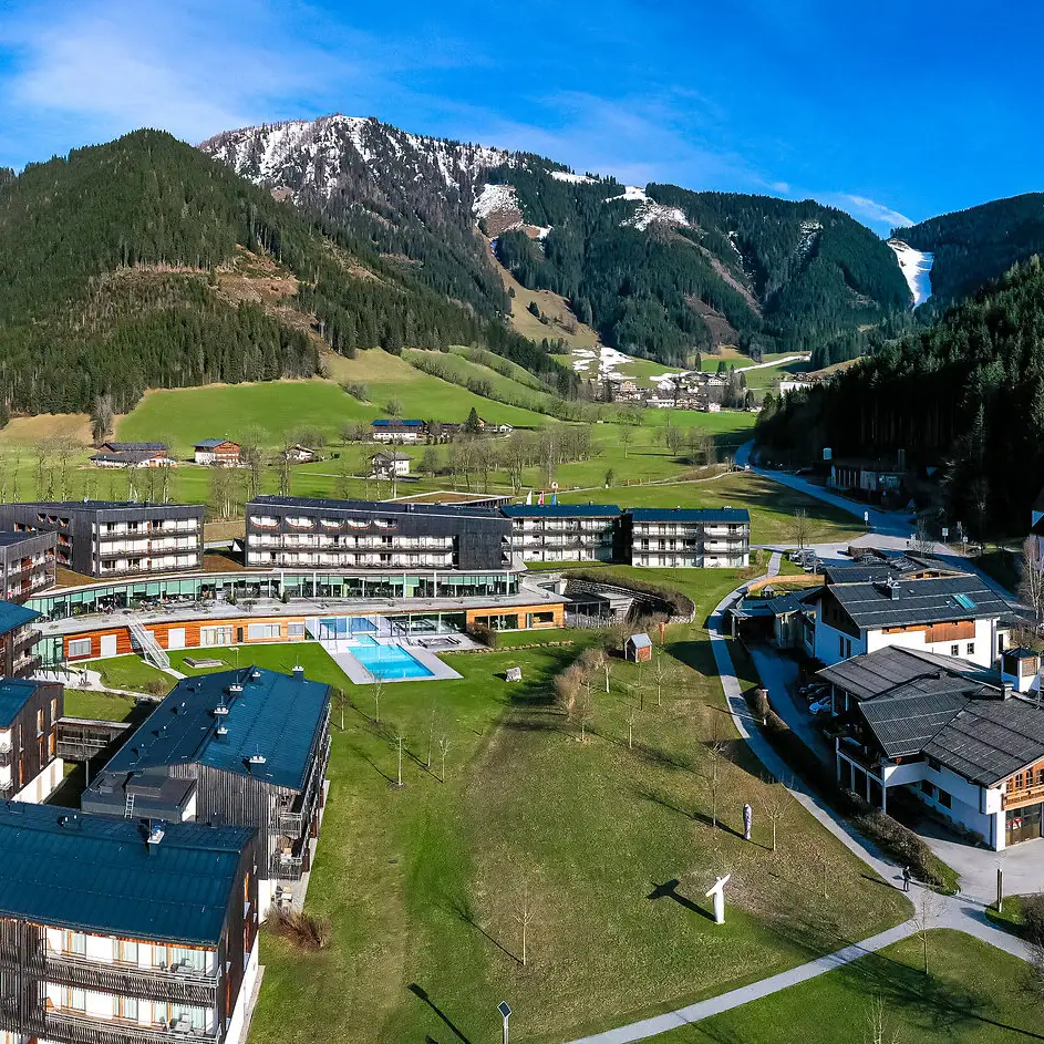 A group of buildings and the hotel with pool in a valley, surrounded by mountains in the background.