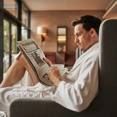 A man in a bathrobe reads a newspaper.