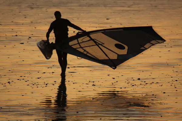 A man holds a sail on the beach.