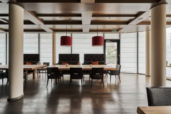 A large room with a wooden floor, large tables and red lamps. The windows around the room are covered with privacy screens. 