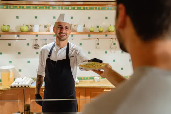 A man in a chef's hat hands another man a plate of food.
