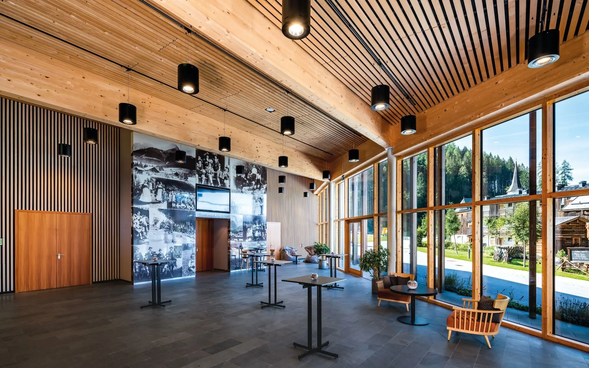A large room with a wide window front, elegant furniture and exposed ceiling beams.