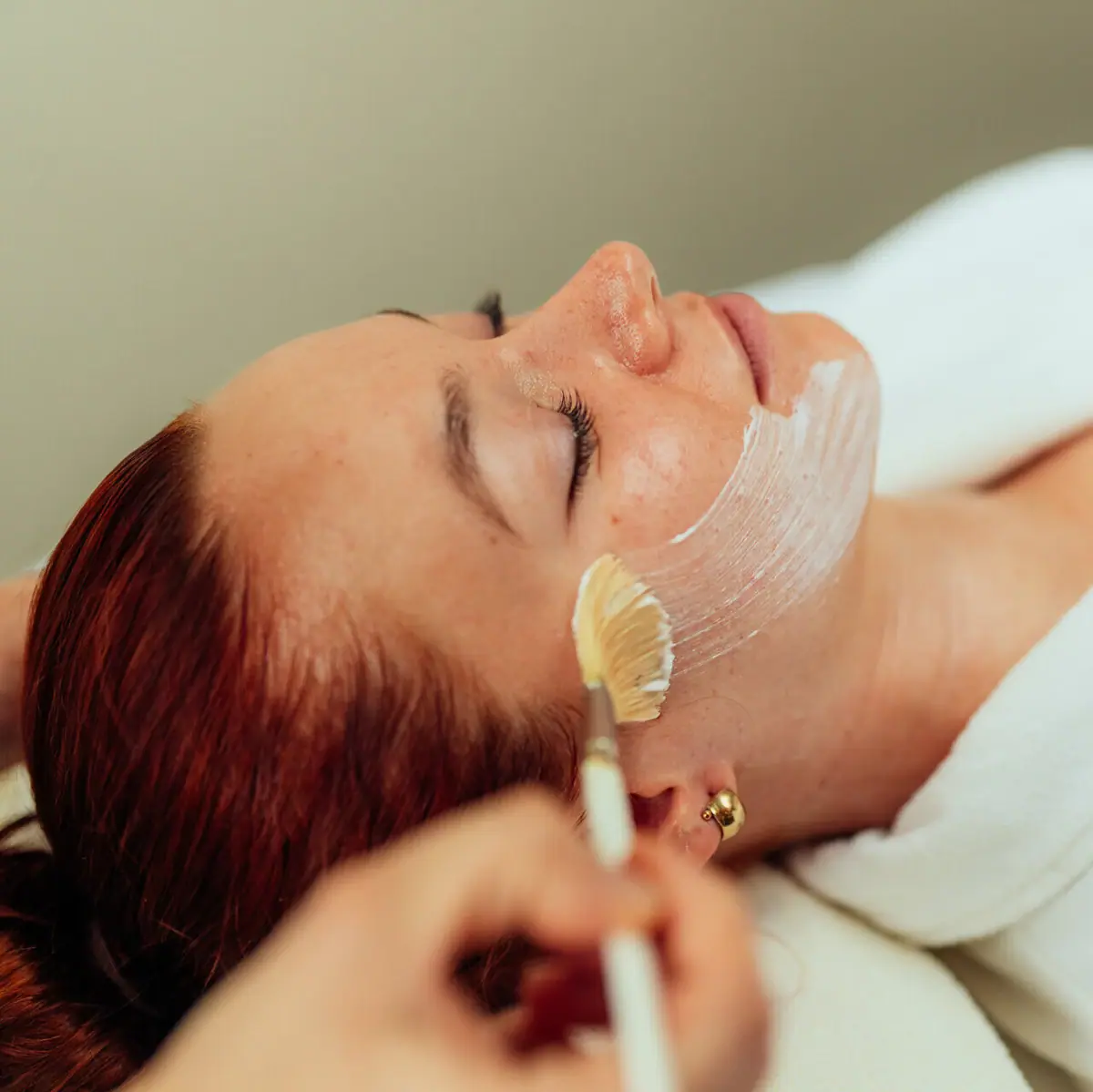 A woman is lying down with a white mask over her face.