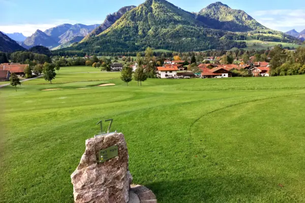 Golf course Ruhpolding A stone in a meadow with a group of houses in the background.