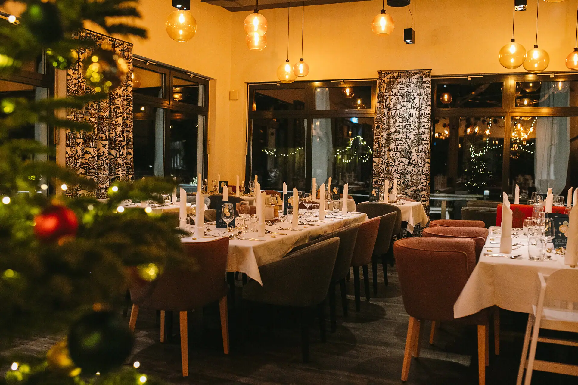 A room with tables and chairs, festively decorated and a Christmas tree in the foreground in the blur.