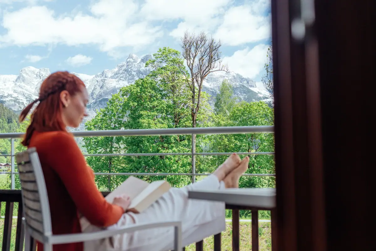 A woman is sitting on a balcony reading a book.