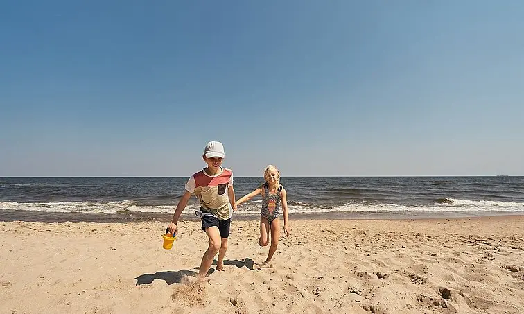 A boy and a girl walk on the beach.