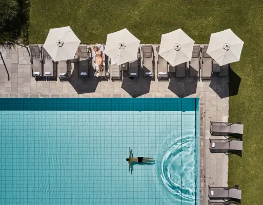 Person swimming in a pool with umbrellas and grass in the background