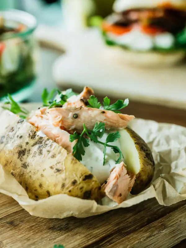 Jacket potato with meat and greens on a wooden board