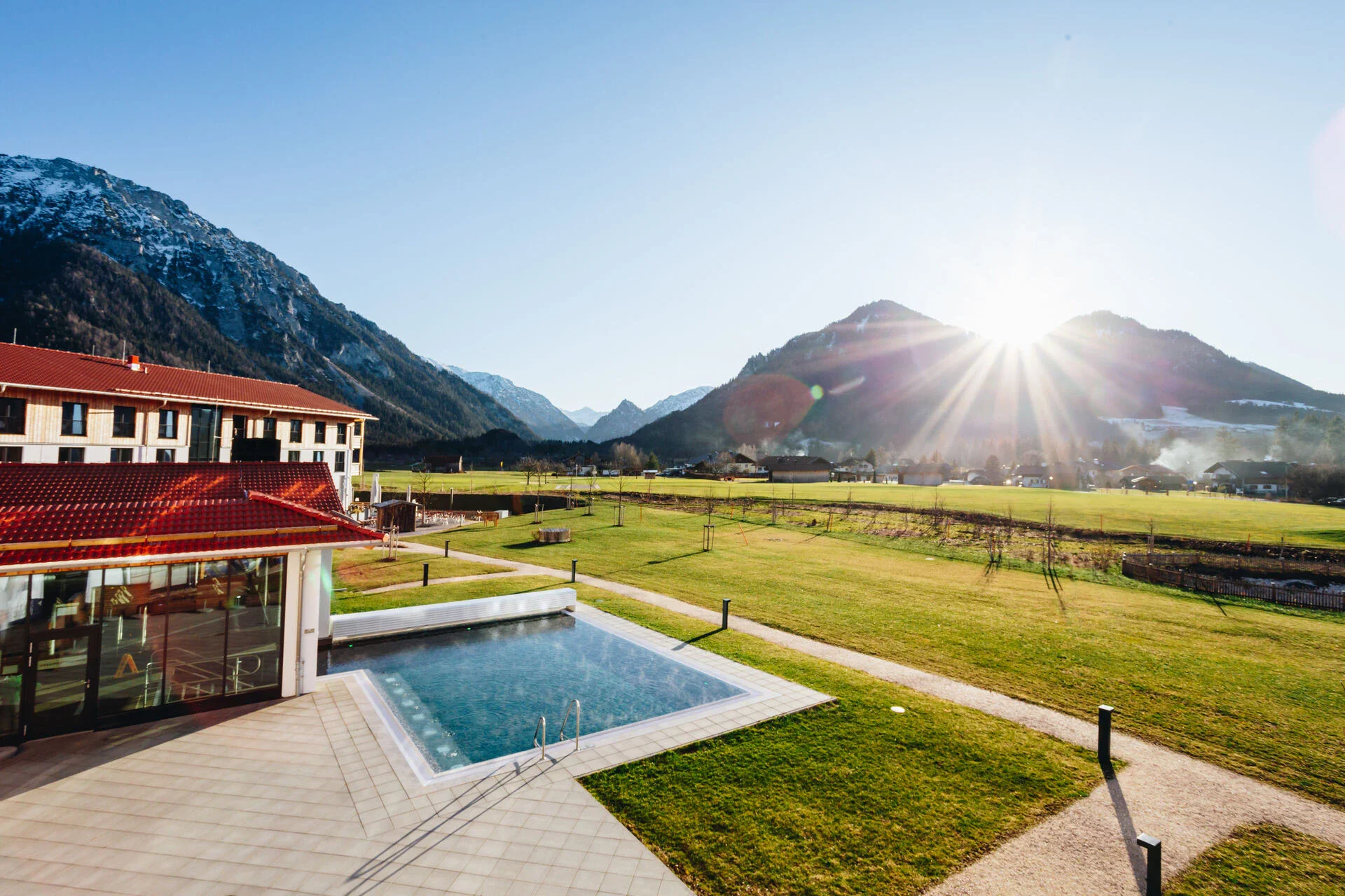 Ein Swimmingpool in einer grasbewachsenen Fläche mit einem Gebäude und Bergen im Hintergrund.
