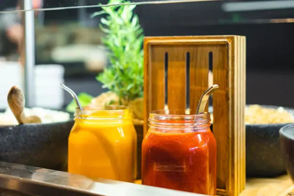 Jars of sauce and a spoon in a wooden holder