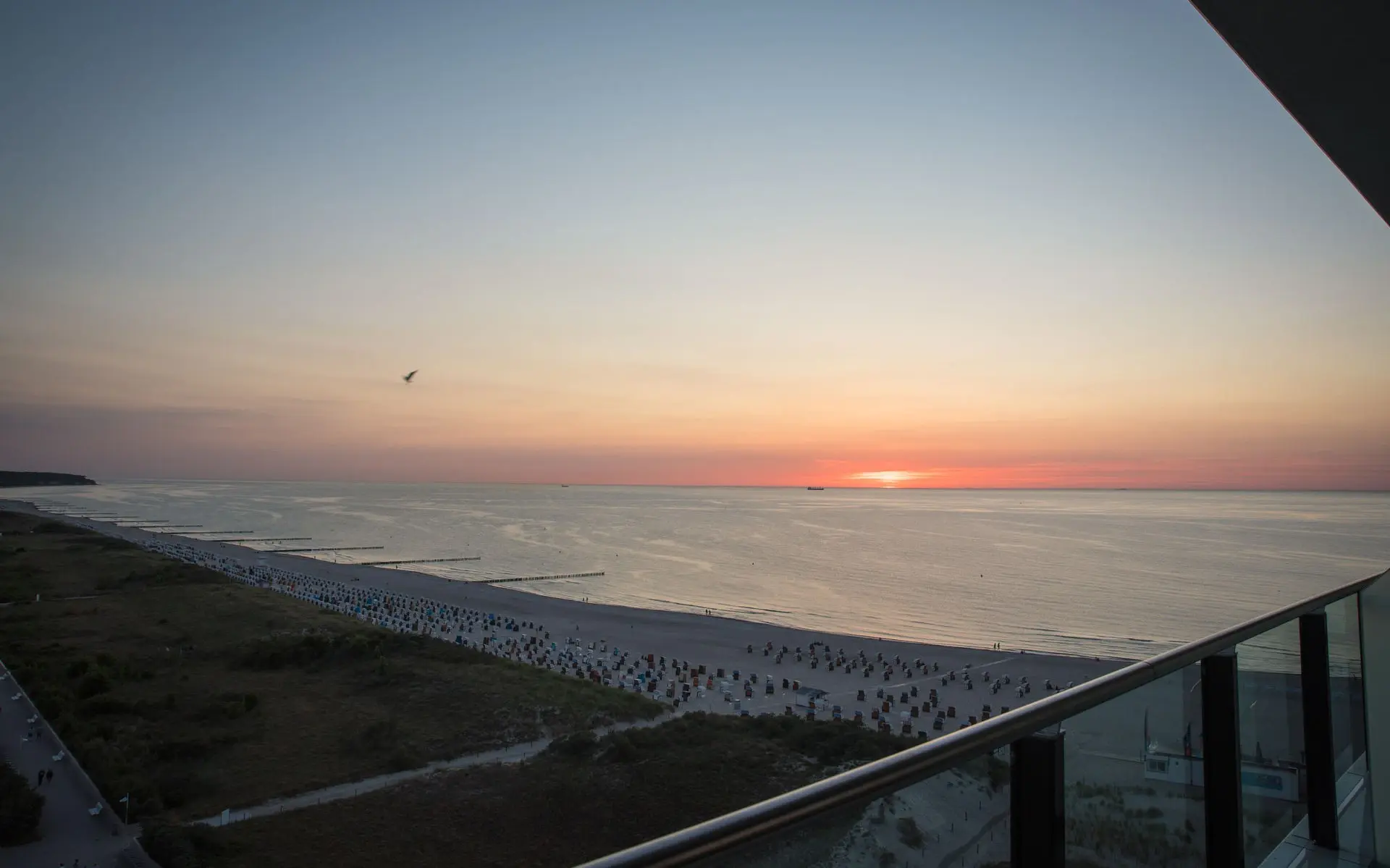 Aerial view of a stretch of beach with the sun setting over the sea in warm colours. 