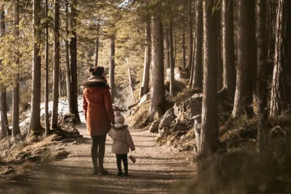 A woman and a child are walking along a forest path.