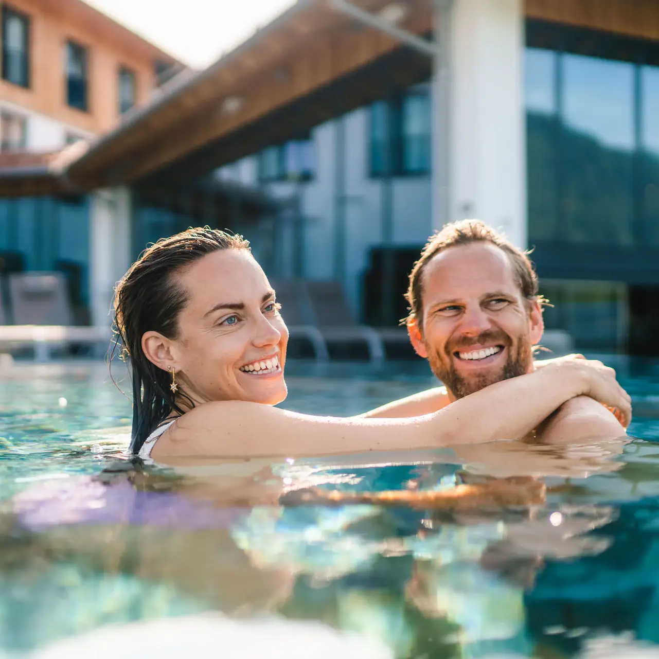 A man and a woman in a pool, smiling in the water.