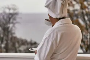 Eine Person im weißen Bademantel mit einem Handtuch auf dem Kopf und einer Tasse Tee.
